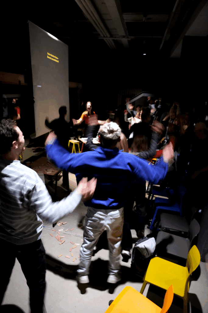 Menschen machen Hampelmänner in einem Veranstaltungsraum vor ihren Sitzstühlen.